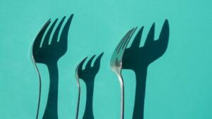 Several silver forks with shadows on a teal background.