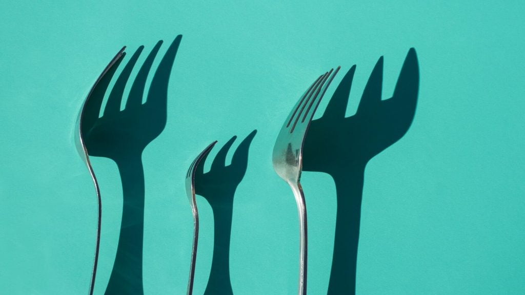 Several silver forks with shadows on a teal background.
