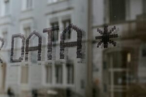 Close up of a window with reflections of buildings. Window has a sign that reads "DATA *"